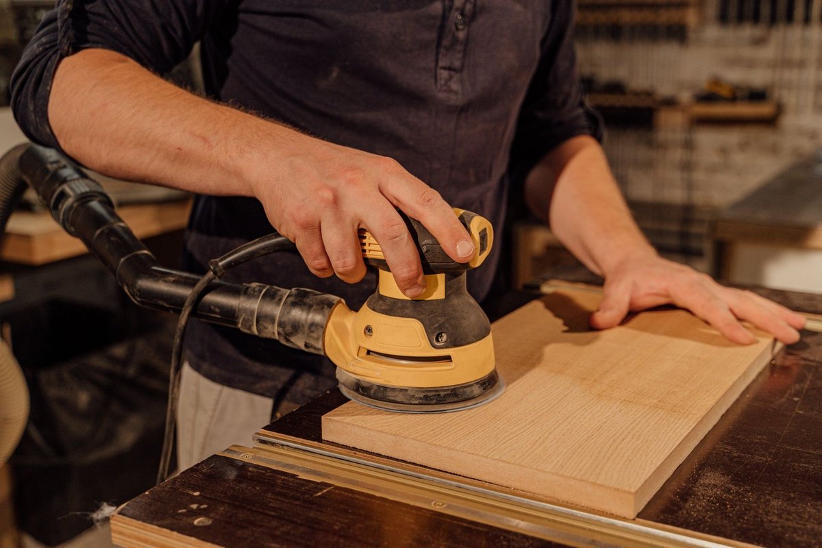 Carpenter sanding a wooden panel with a power sander on a workbench