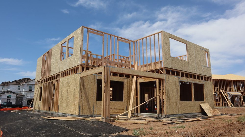 Two story house at the framing stage with wall sheathing in place under a blue sky