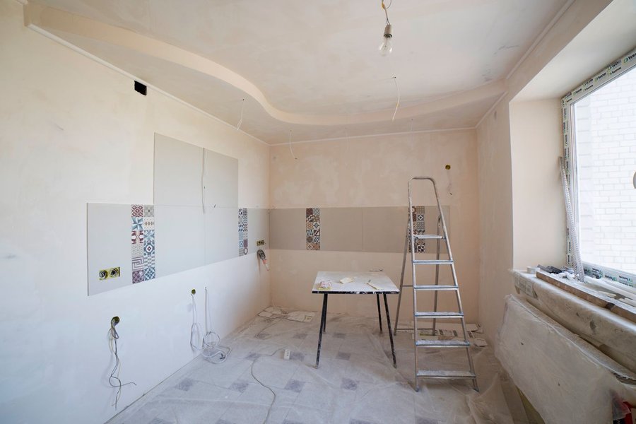 Room mid renovation with a step ladder, bare walls, and materials staged on the floor